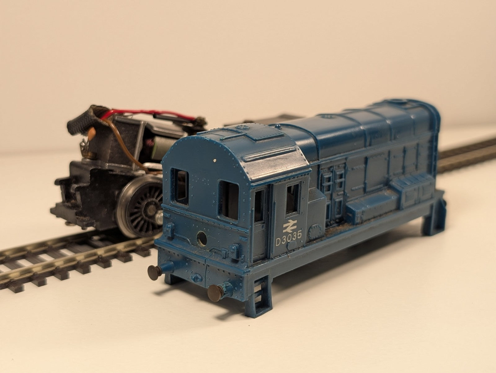 Blue model train engine D3035 on tracks, with a black engine chassis behind it